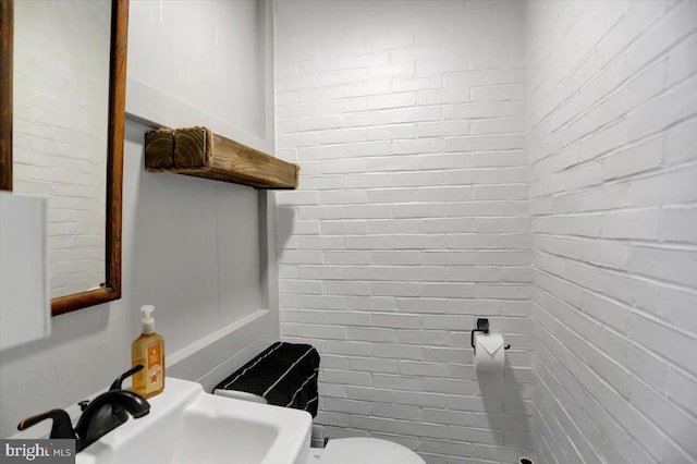 half bathroom featuring toilet, brick wall, and a sink