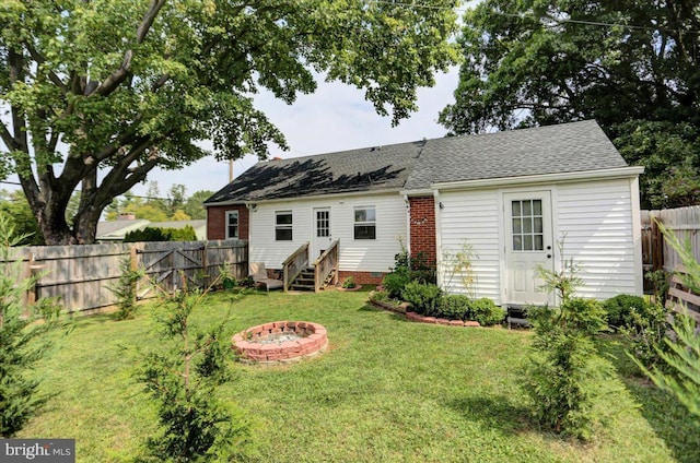 rear view of house with entry steps, an outdoor fire pit, a fenced backyard, a yard, and brick siding