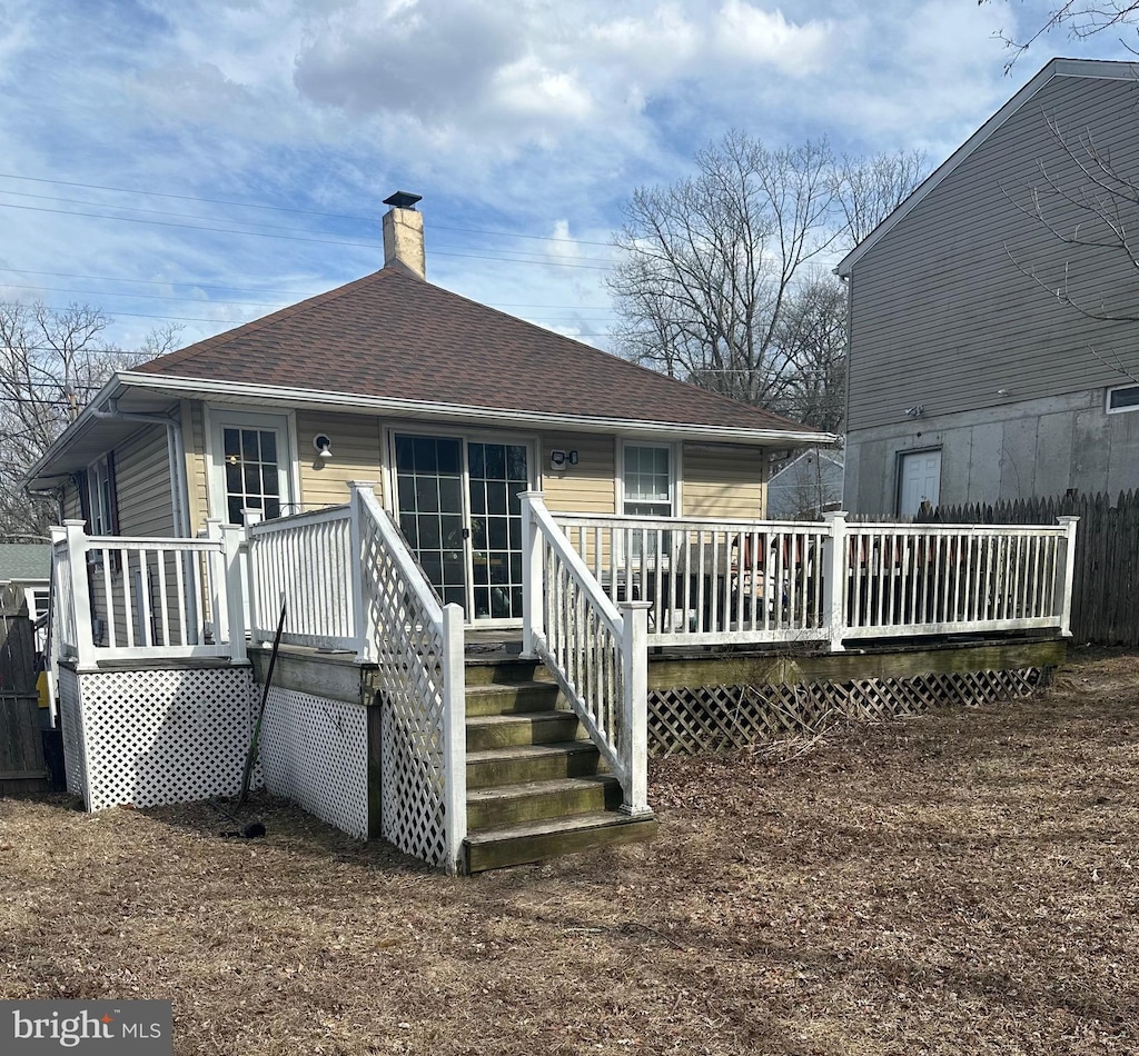 back of house featuring roof with shingles, a chimney, and a wooden deck