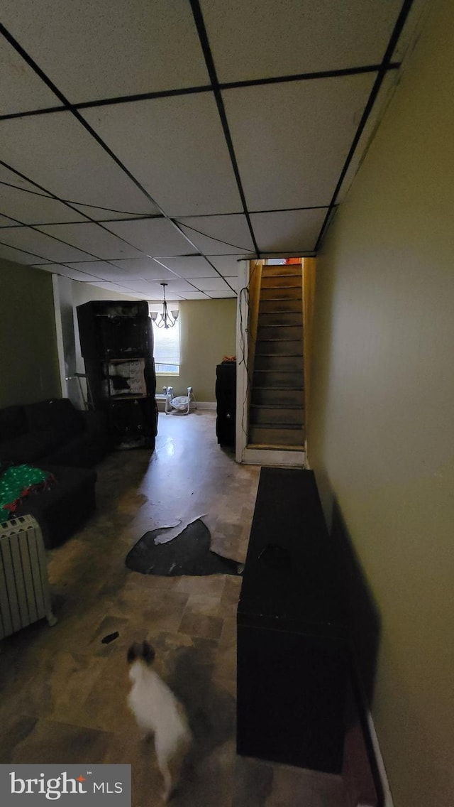 basement with radiator heating unit, stairway, and a paneled ceiling