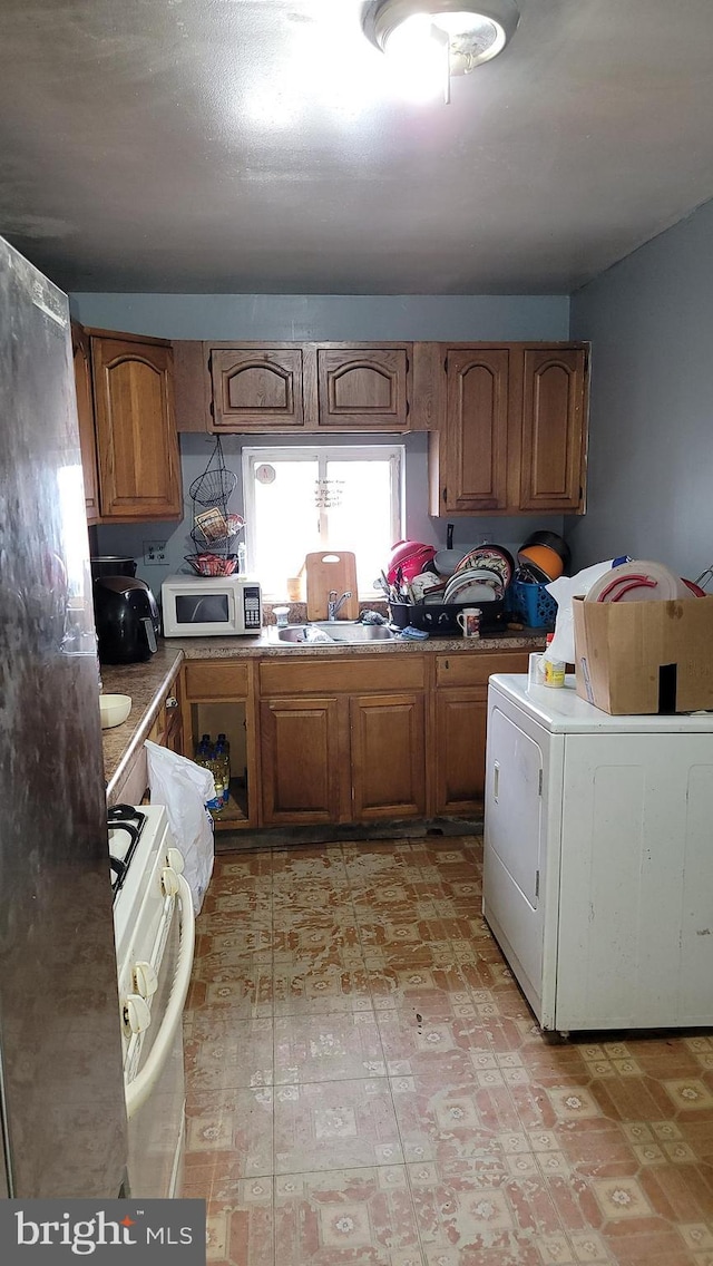 kitchen with white appliances, brown cabinetry, a sink, and washer / dryer