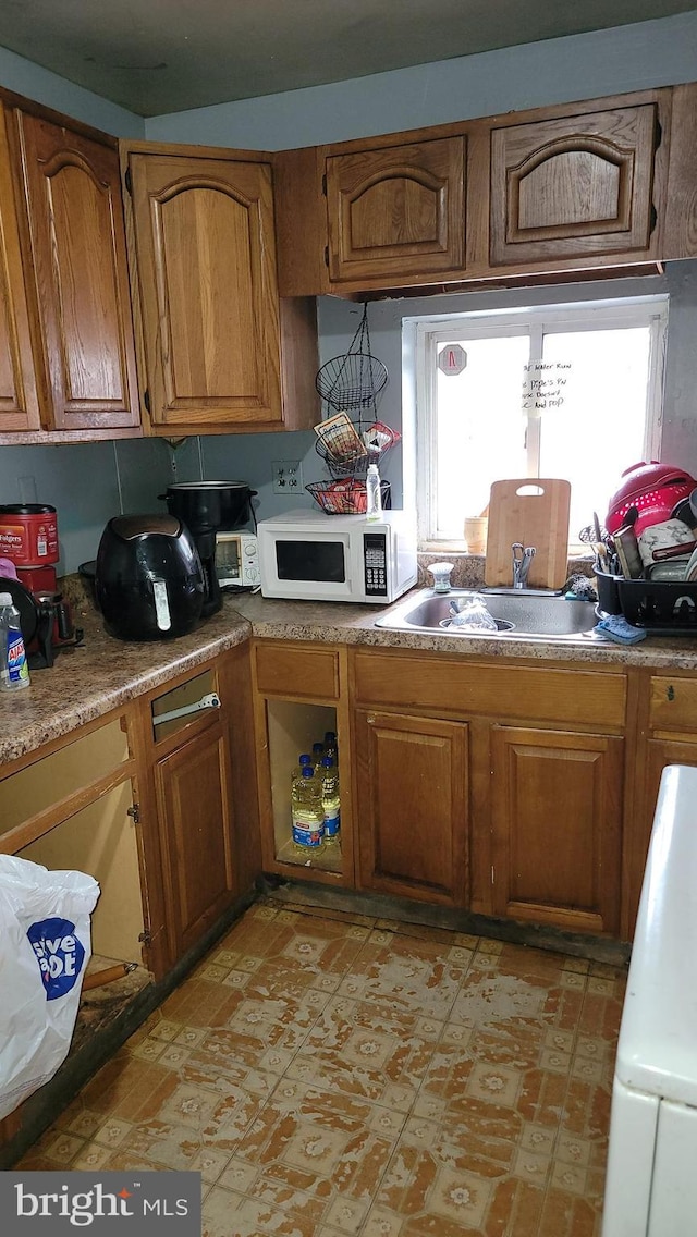 kitchen featuring brown cabinets, a sink, and white microwave