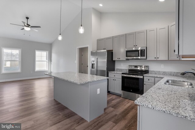 kitchen with stainless steel appliances, a kitchen island, a sink, light stone countertops, and dark wood-style floors