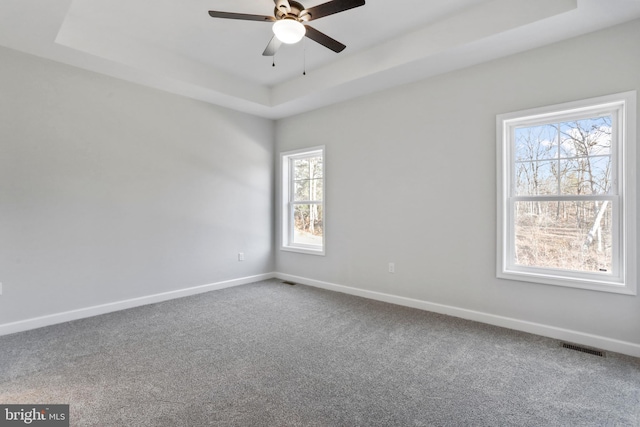 empty room with a tray ceiling, carpet flooring, visible vents, and baseboards