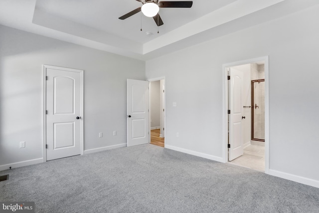 unfurnished bedroom featuring a tray ceiling, carpet flooring, connected bathroom, and baseboards