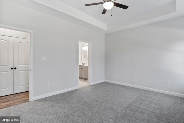 unfurnished bedroom featuring baseboards, ceiling fan, a tray ceiling, carpet floors, and a closet