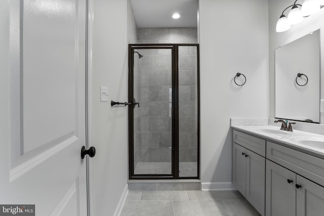 bathroom with double vanity, a shower stall, baseboards, and a sink