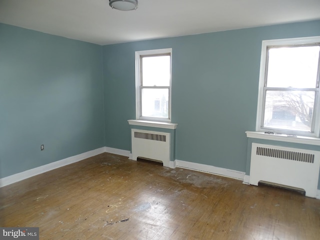 spare room with a healthy amount of sunlight, hardwood / wood-style flooring, and radiator