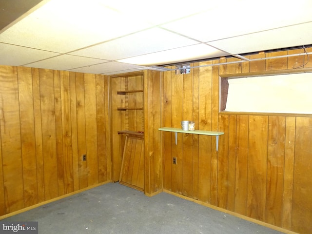 finished basement featuring a drop ceiling and wooden walls