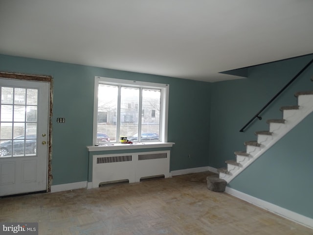 entrance foyer with baseboards, radiator heating unit, and stairs