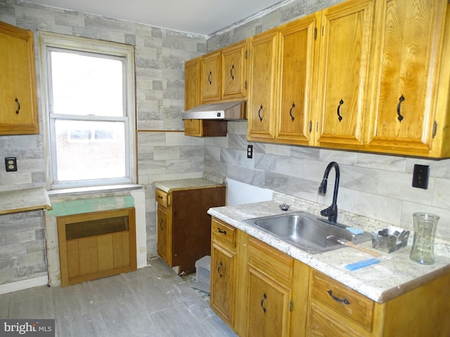 kitchen featuring brown cabinets, light countertops, a sink, and under cabinet range hood