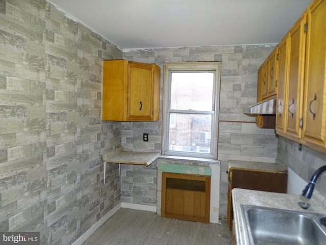 kitchen with brown cabinetry, light countertops, a sink, and tile walls