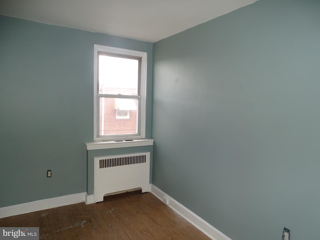 empty room with baseboards, radiator heating unit, and wood finished floors