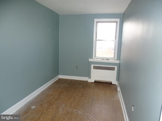 unfurnished room with radiator, wood-type flooring, and baseboards