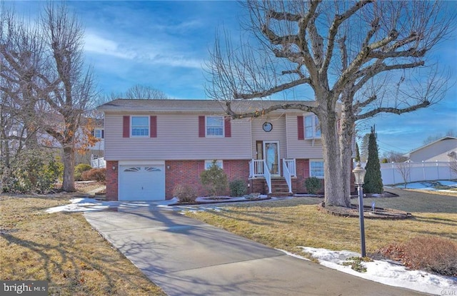 split foyer home with a garage, brick siding, fence, driveway, and a front yard