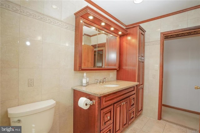 half bath with toilet, tile patterned floors, crown molding, vanity, and tile walls