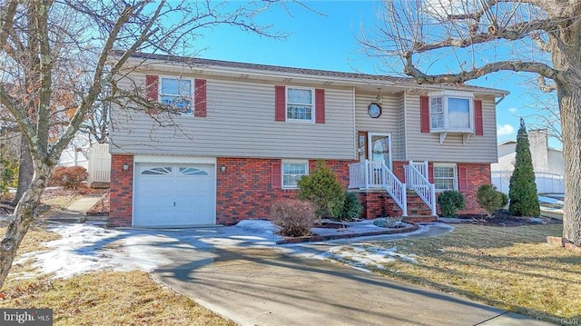 raised ranch with driveway, brick siding, and an attached garage