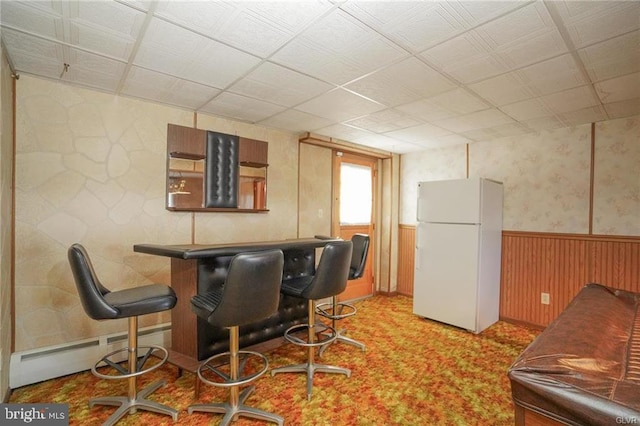 kitchen featuring a wainscoted wall, wooden walls, baseboard heating, and freestanding refrigerator