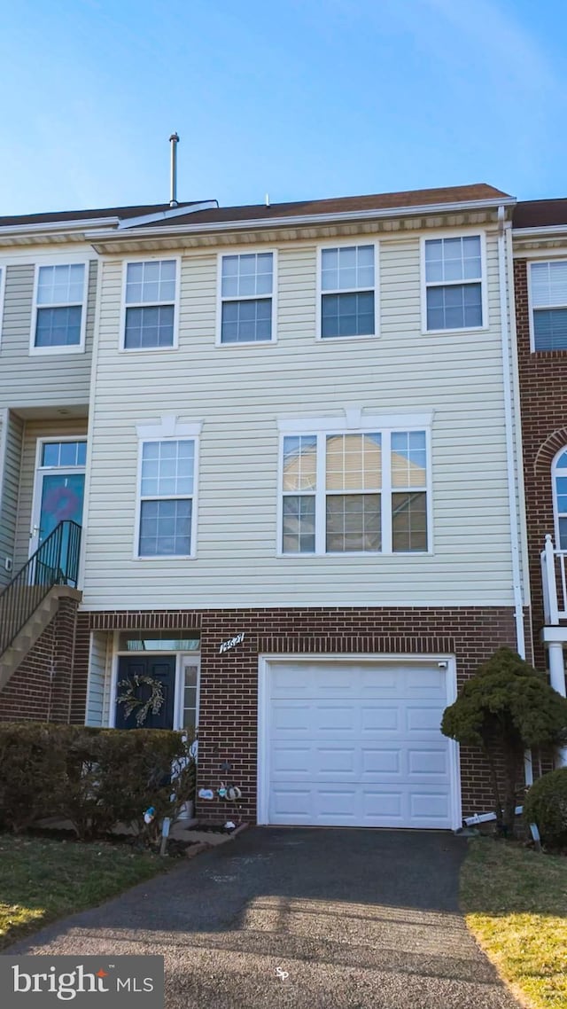 view of property with brick siding, an attached garage, and driveway