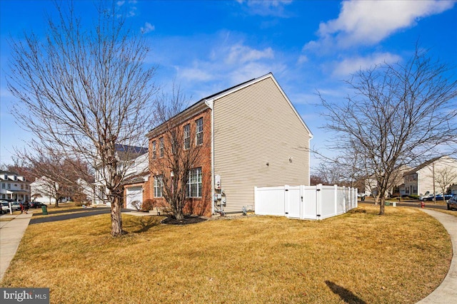 view of property exterior featuring brick siding, fence, a lawn, and driveway