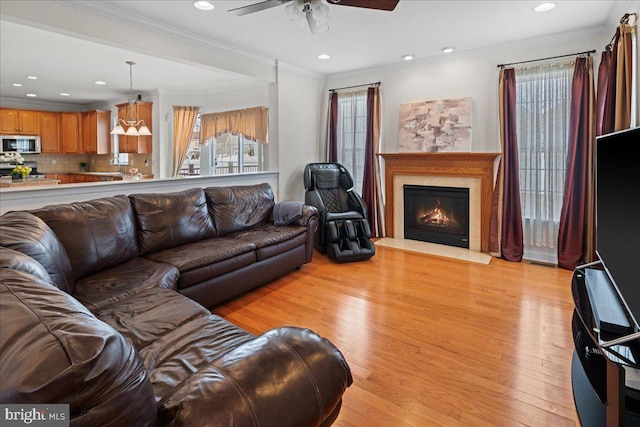 living room featuring recessed lighting, ceiling fan, a lit fireplace, light wood-style floors, and crown molding