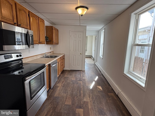 kitchen featuring dark wood-style floors, stainless steel appliances, brown cabinetry, a sink, and a drop ceiling