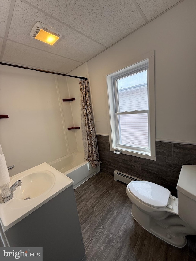 full bath with shower / bathtub combination with curtain, toilet, wainscoting, wood finished floors, and a drop ceiling