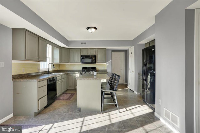 kitchen with a kitchen bar, black appliances, visible vents, and a sink