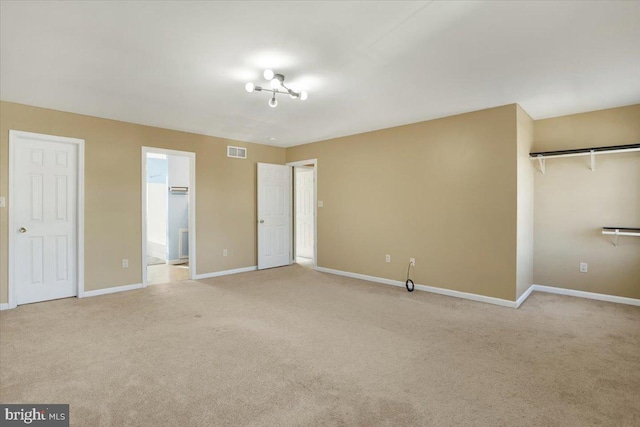 unfurnished bedroom featuring baseboards, visible vents, ensuite bath, a closet, and light carpet