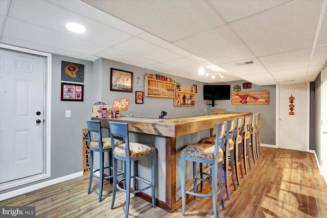 bar featuring indoor wet bar, wood finished floors, baseboards, and a drop ceiling