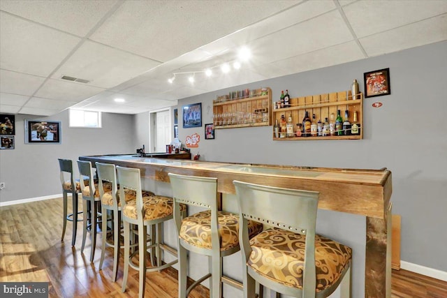 bar featuring visible vents, a paneled ceiling, baseboards, and wood finished floors