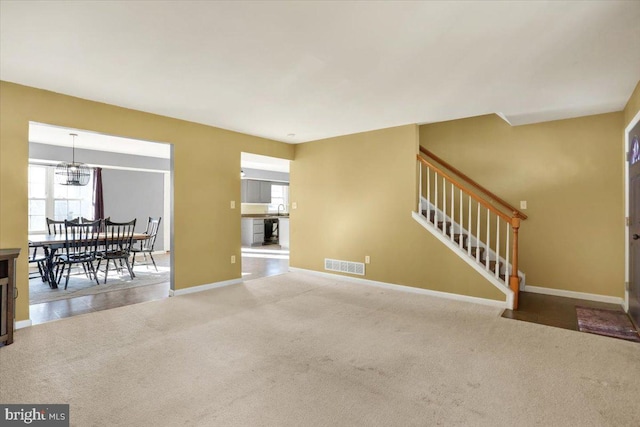 carpeted living area featuring a chandelier, visible vents, stairs, and baseboards