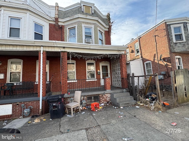 view of front of property featuring cooling unit, covered porch, brick siding, and fence