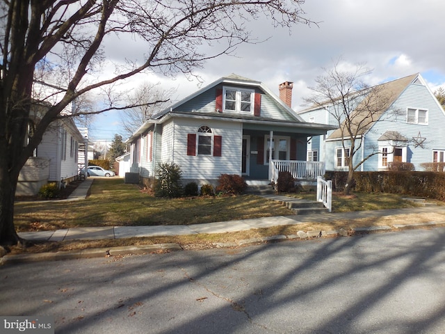 bungalow-style house featuring a porch, a chimney, and a front lawn