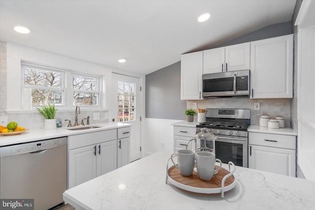 kitchen with white cabinets, appliances with stainless steel finishes, vaulted ceiling, and a sink