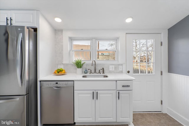 kitchen featuring white cabinetry, stainless steel appliances, a sink, and wainscoting