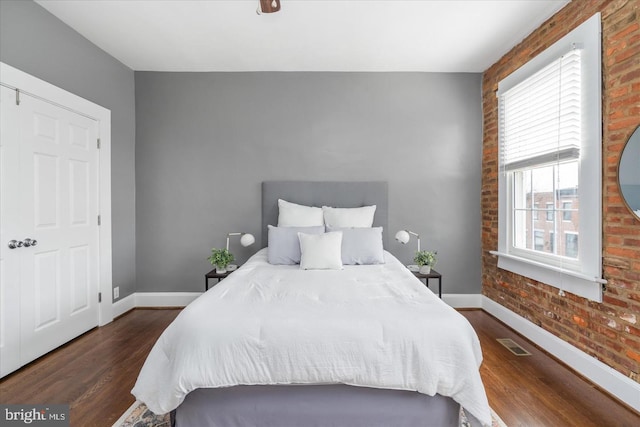 bedroom with brick wall, baseboards, visible vents, and wood finished floors