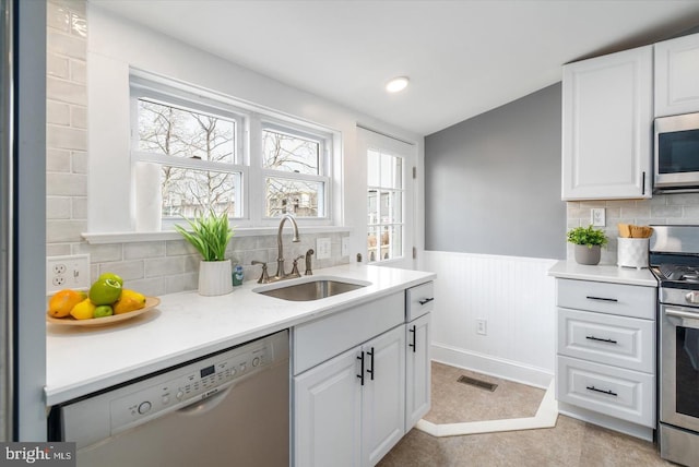 kitchen featuring white cabinets, wainscoting, appliances with stainless steel finishes, light countertops, and a sink