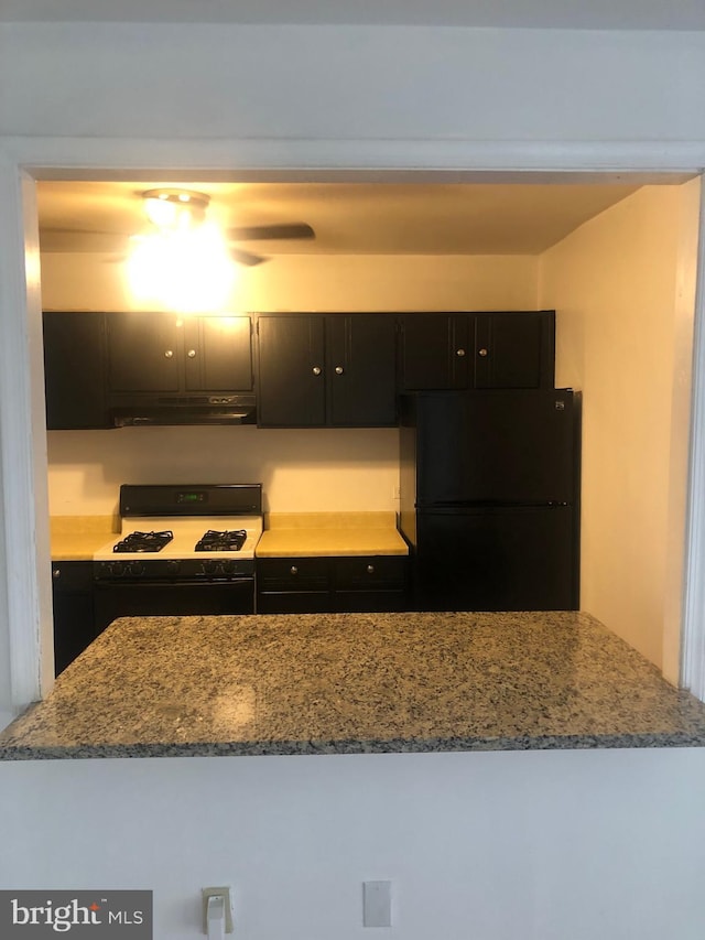 kitchen featuring stone counters, range with gas cooktop, freestanding refrigerator, dark cabinets, and under cabinet range hood