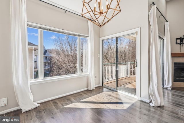 unfurnished dining area featuring an inviting chandelier, a healthy amount of sunlight, baseboards, and wood finished floors