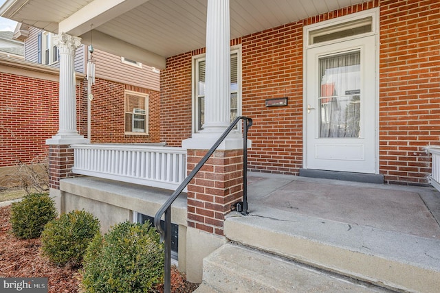 view of exterior entry featuring a porch and brick siding