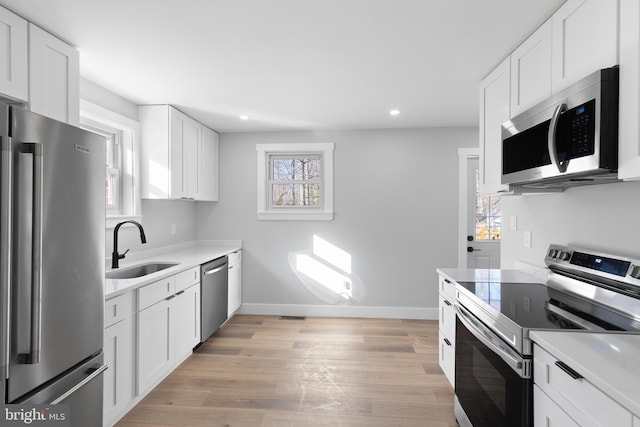 kitchen with light wood finished floors, appliances with stainless steel finishes, light countertops, and a sink