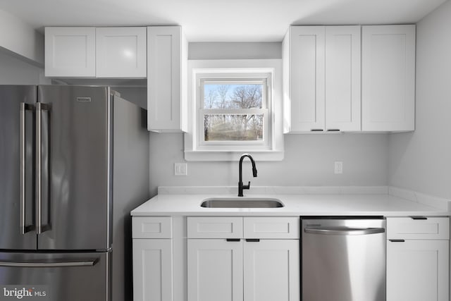 kitchen featuring stainless steel appliances, light countertops, a sink, and white cabinetry