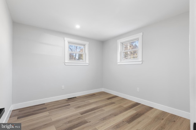 empty room with visible vents, plenty of natural light, baseboards, and wood finished floors