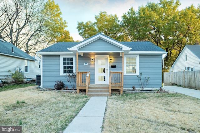 bungalow-style home featuring a shingled roof, a front yard, and fence