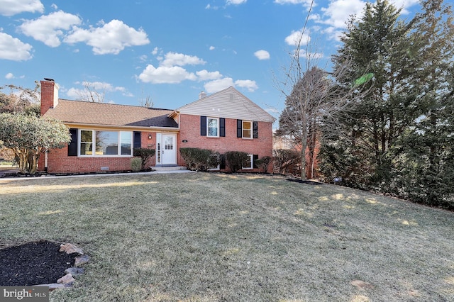 split level home with brick siding, a chimney, and a front yard