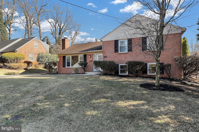 tri-level home featuring brick siding, a chimney, and a front yard