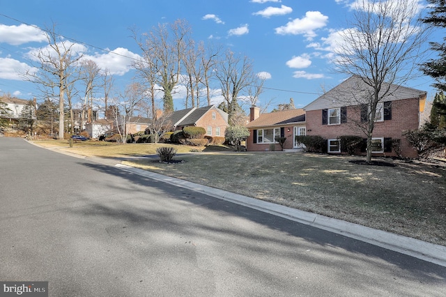 tri-level home featuring brick siding, a residential view, a chimney, and a front yard