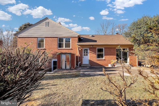 back of house with brick siding, entry steps, a chimney, and roof with shingles