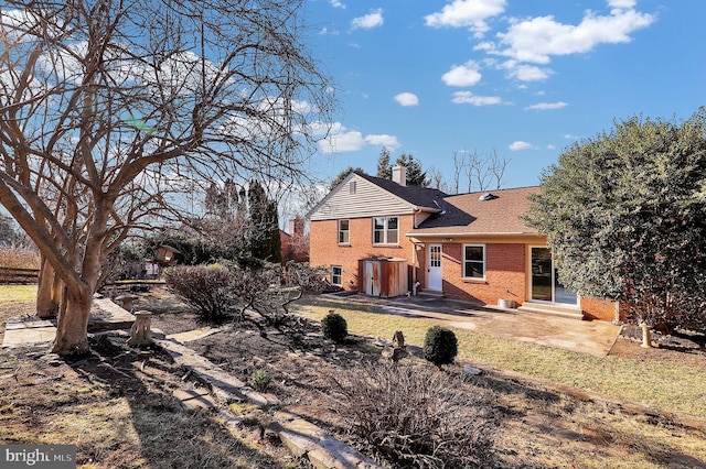 rear view of property featuring a shingled roof, entry steps, a chimney, a patio area, and brick siding